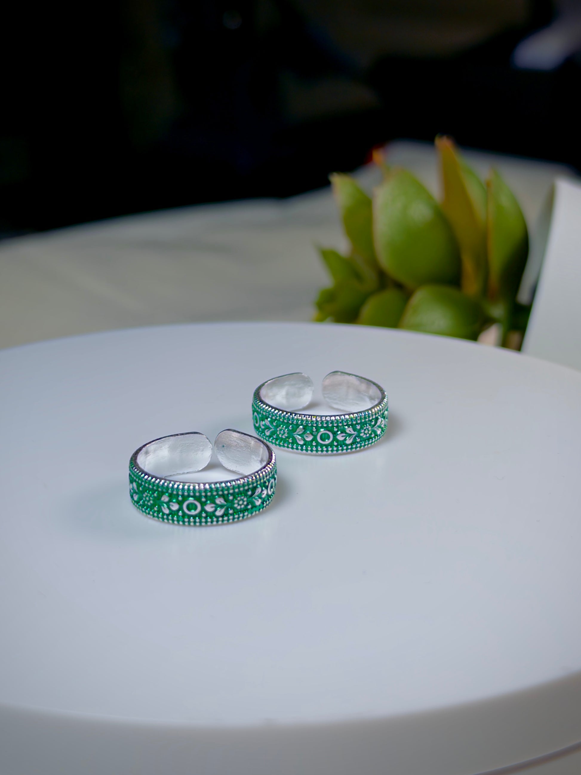 Pair of green and silver toe rings on a white surface with a blurred background