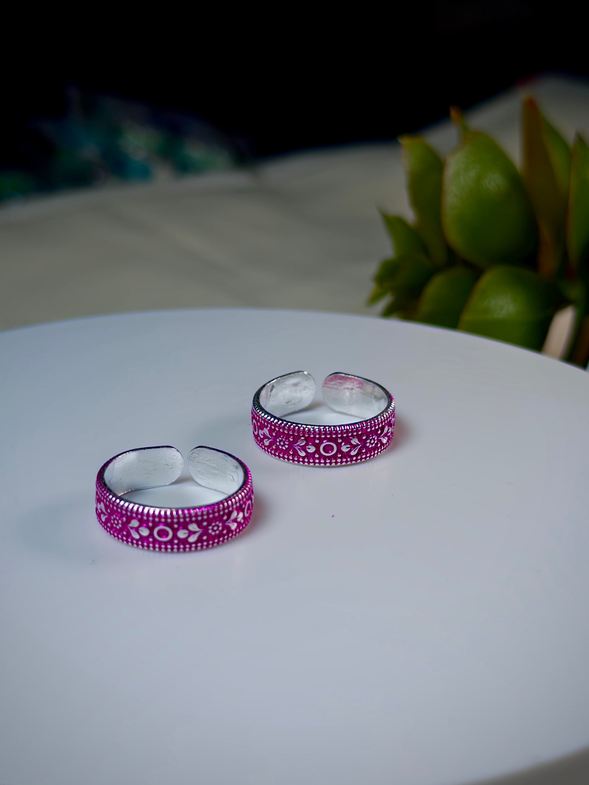Pair of silver and pink toe rings on a white surface with a blurred background