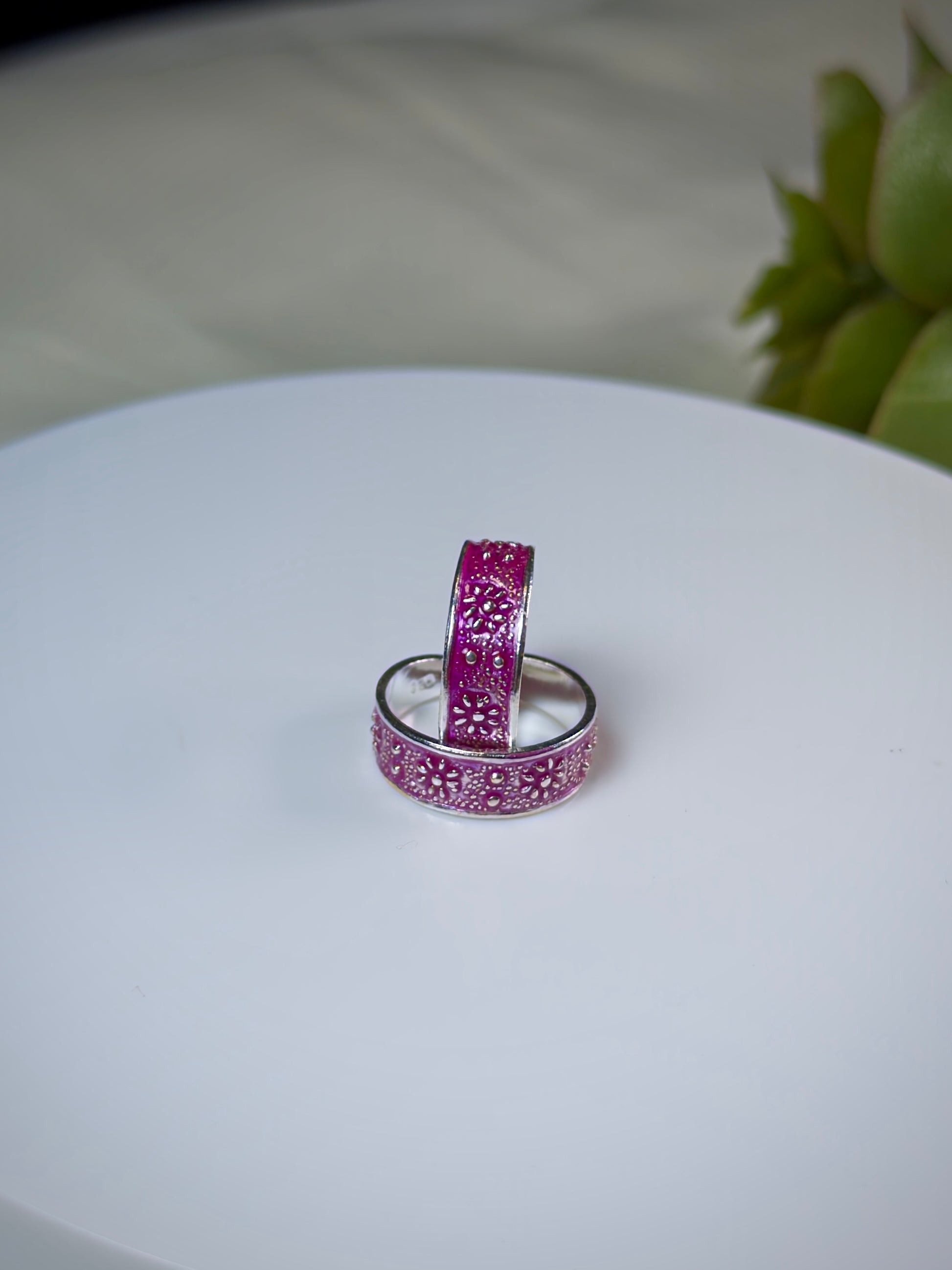 Two pink toe rings with intricate designs on a white surface.