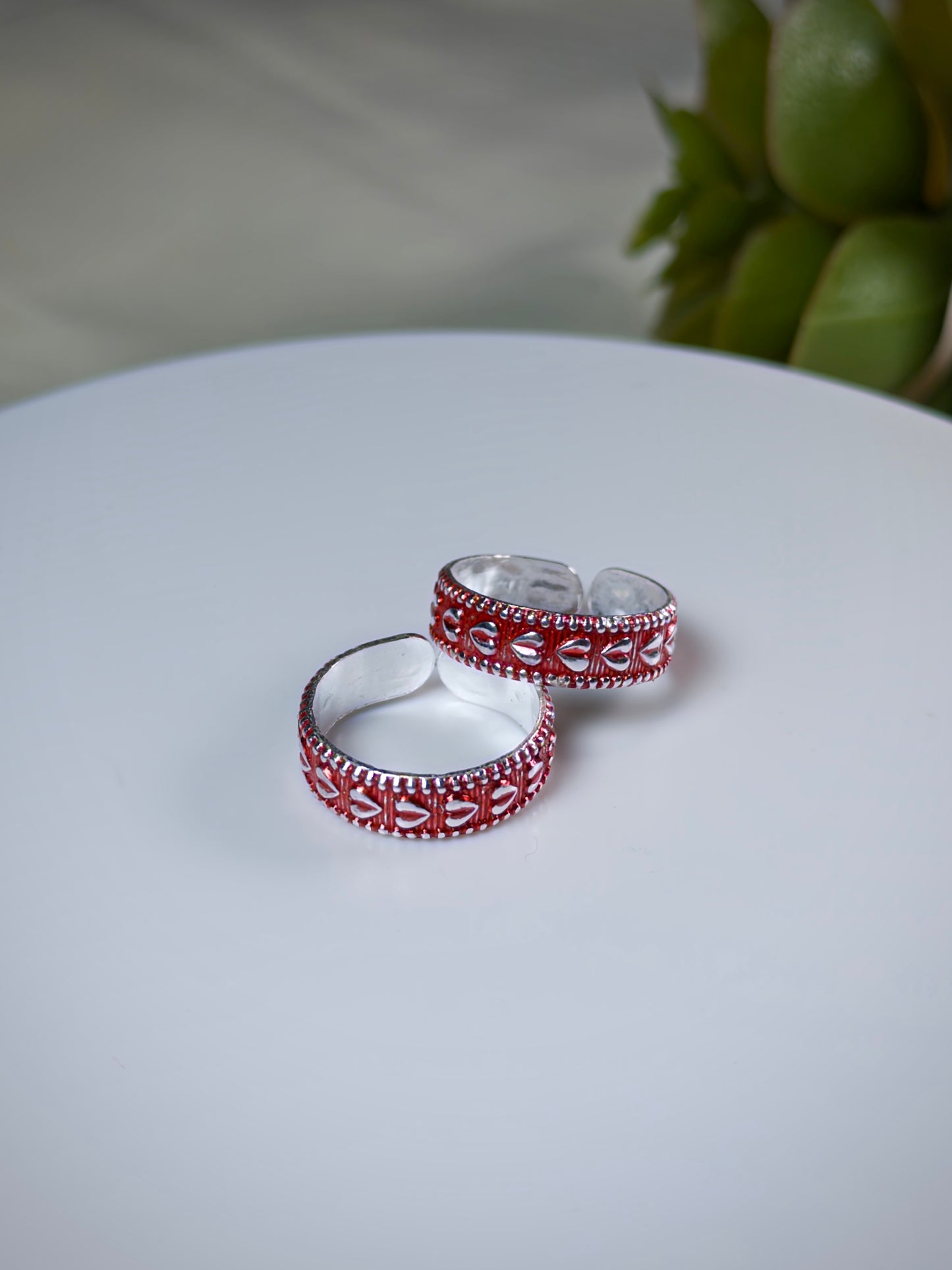 Two silver toe rings with red accents on a white surface.