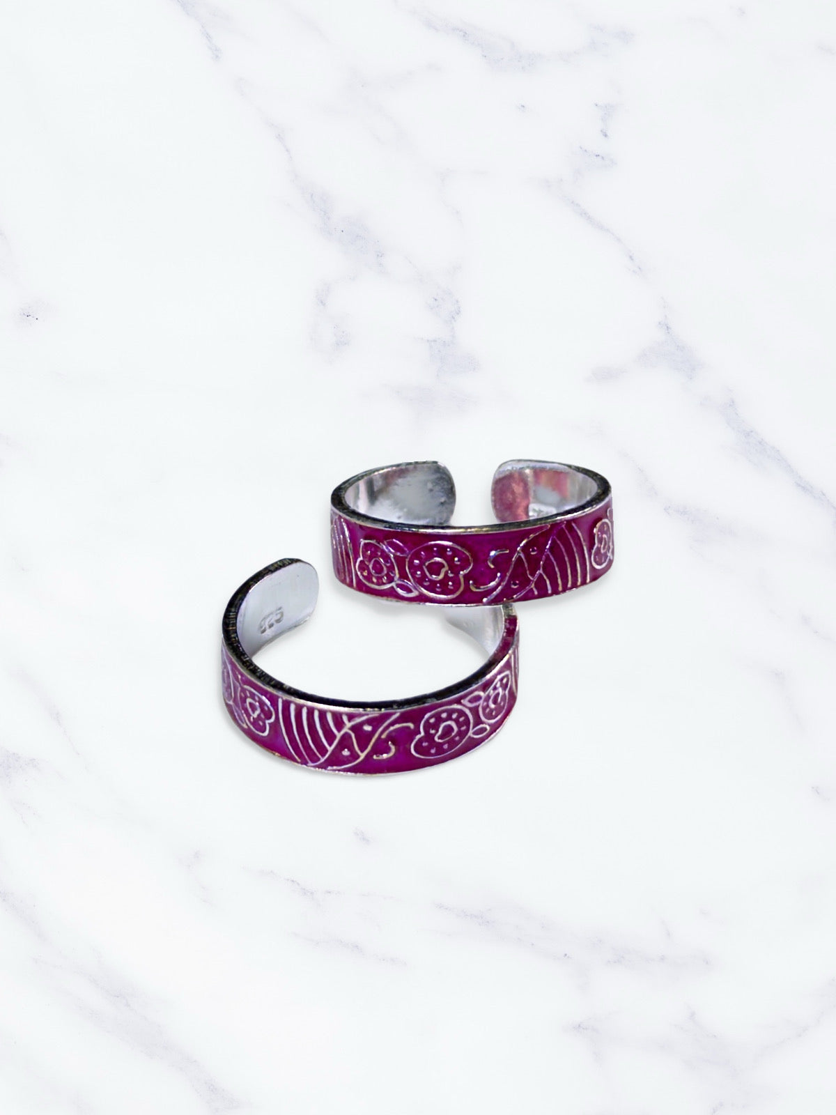 Two pink toe rings with intricate designs on a white marble surface