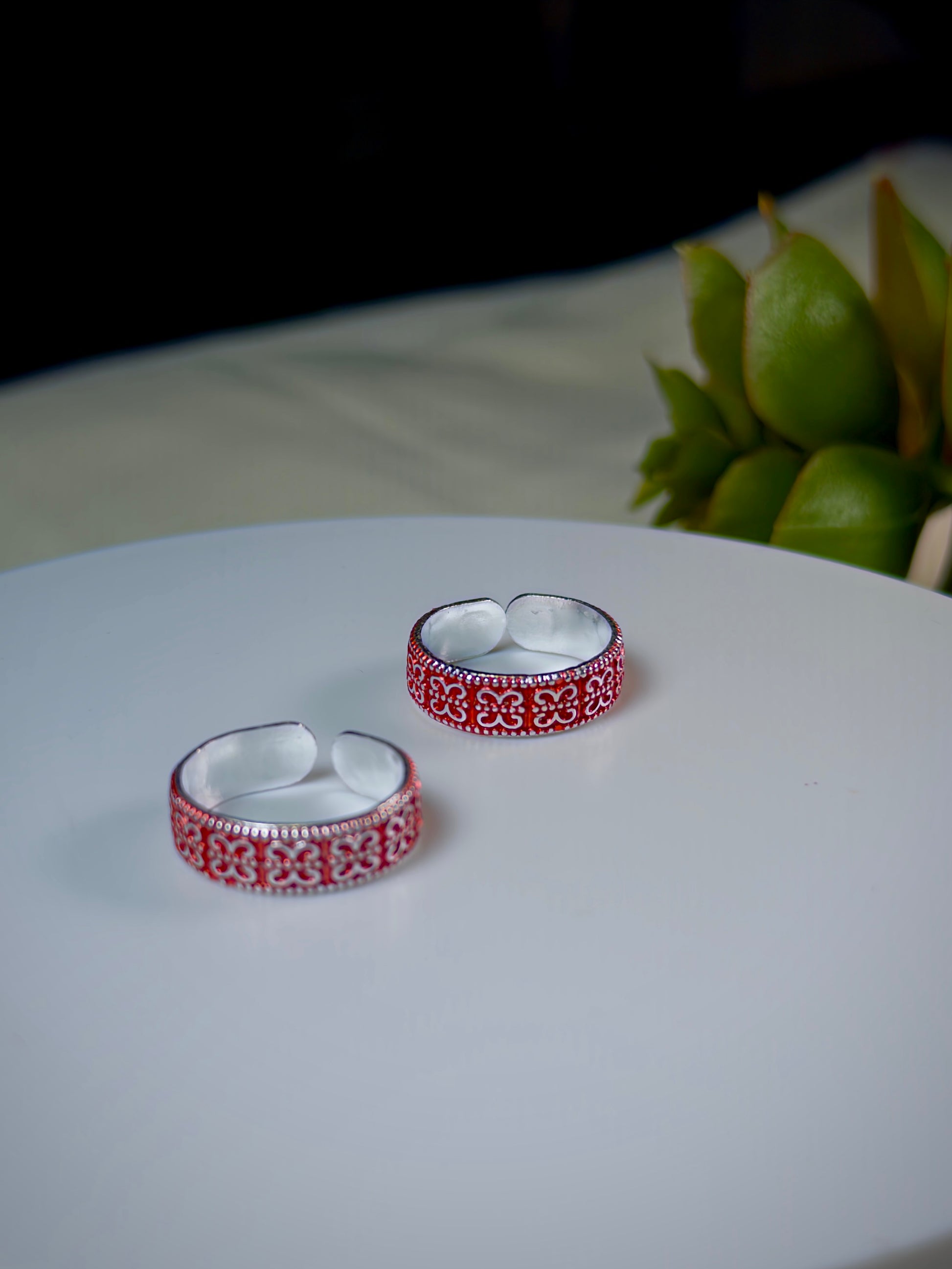 Two silver toe rings with red patterns on a white surface with a blurred background