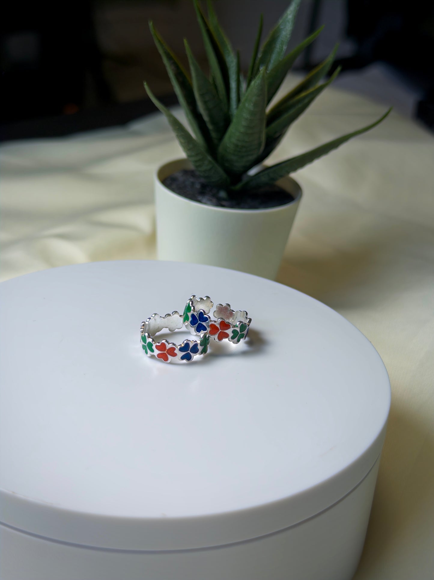 Colorful floral toe rings on a white box with a potted plant in the background