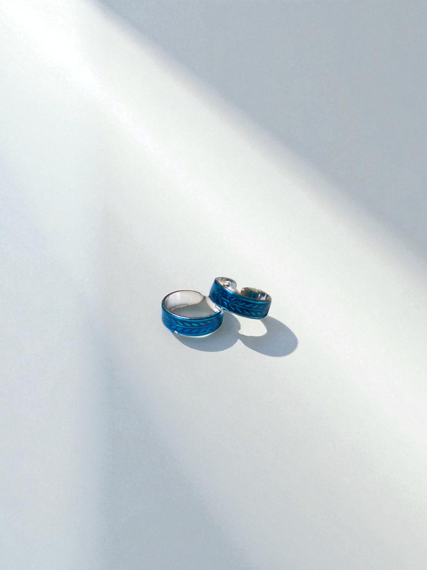 Two blue toe rings on a white surface with a soft shadow