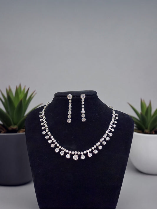 Silver necklace and earrings on a black mannequin bust with plants in the background