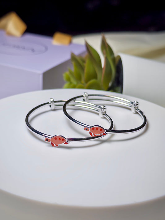 Silver baby kada with red turtle designs on a white plate