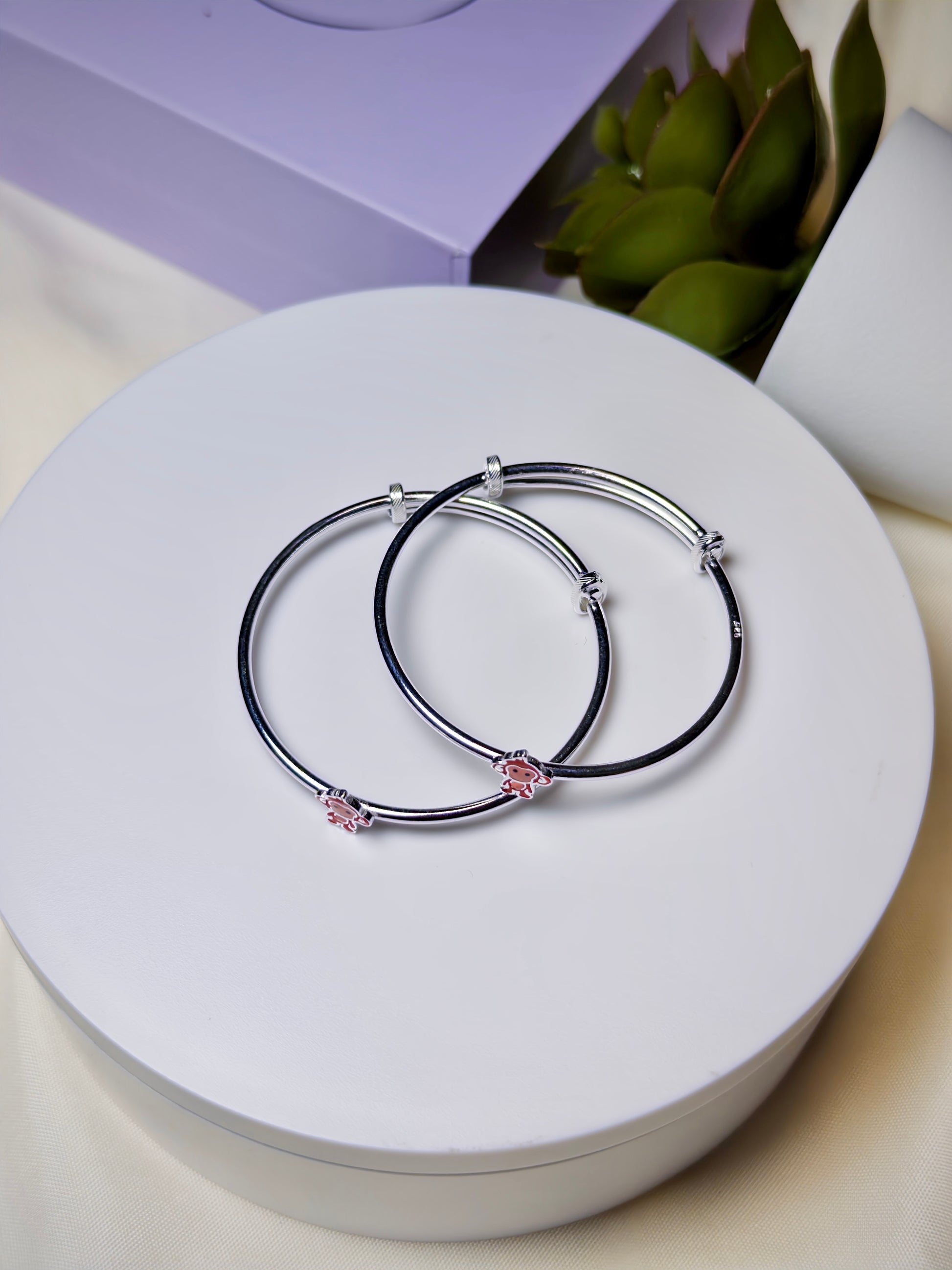 Two silver baby kada with pink monkey charms on a white surface.