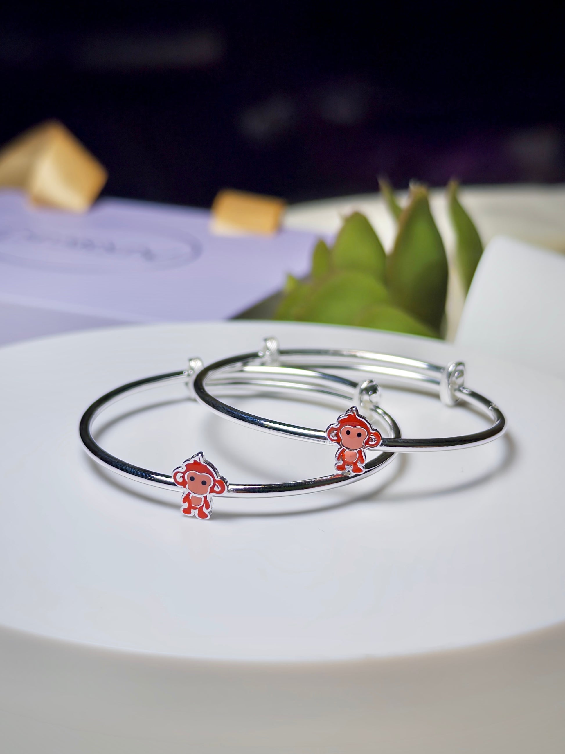 Silver baby kada with monkey charms on a white plate