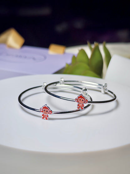 Silver baby kada with monkey charms on a white plate