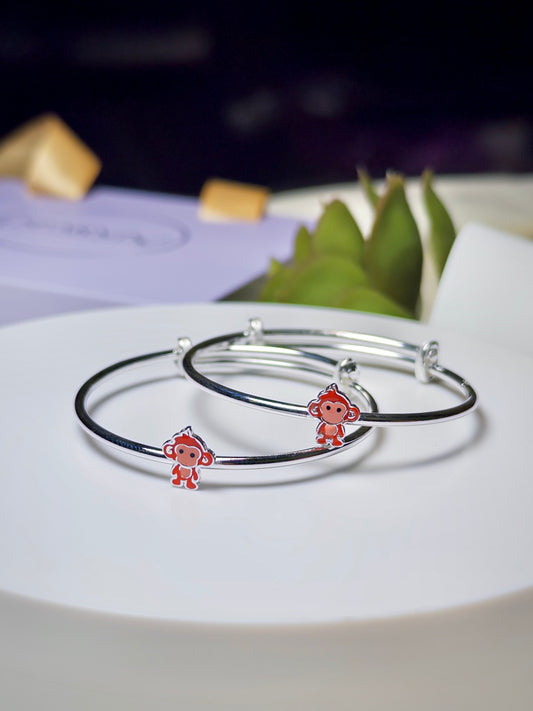Silver baby kada with monkey charms on a white plate
