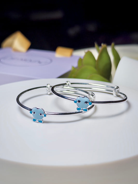 Two silver baby kada with blue cartoon character charms on a white surface.