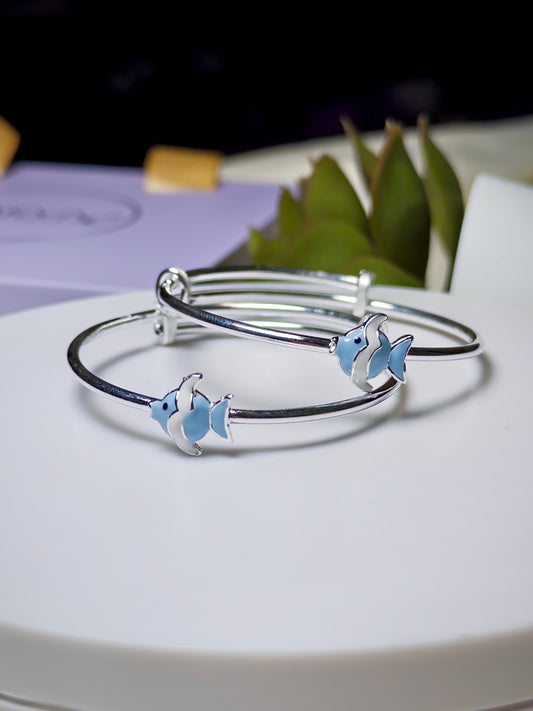 Silver baby kada with blue fish charms on a white surface