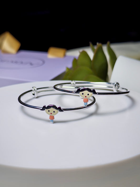 Silver baby kada with character charms on a white surface