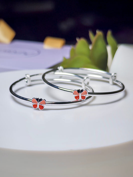 Silver baby kada with red butterfly charms on a white surface