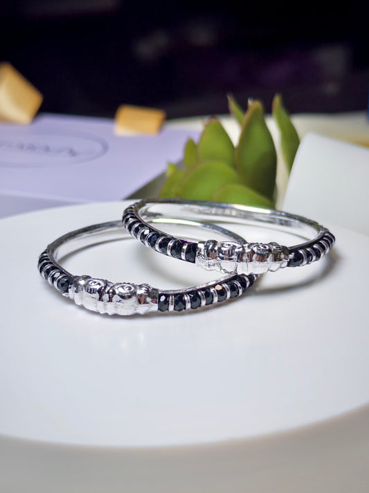 Two silver bracelets with black accents on a white surface