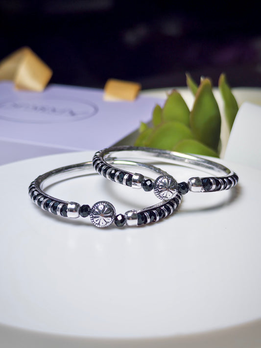 Silver baby kada with black beads on a white surface