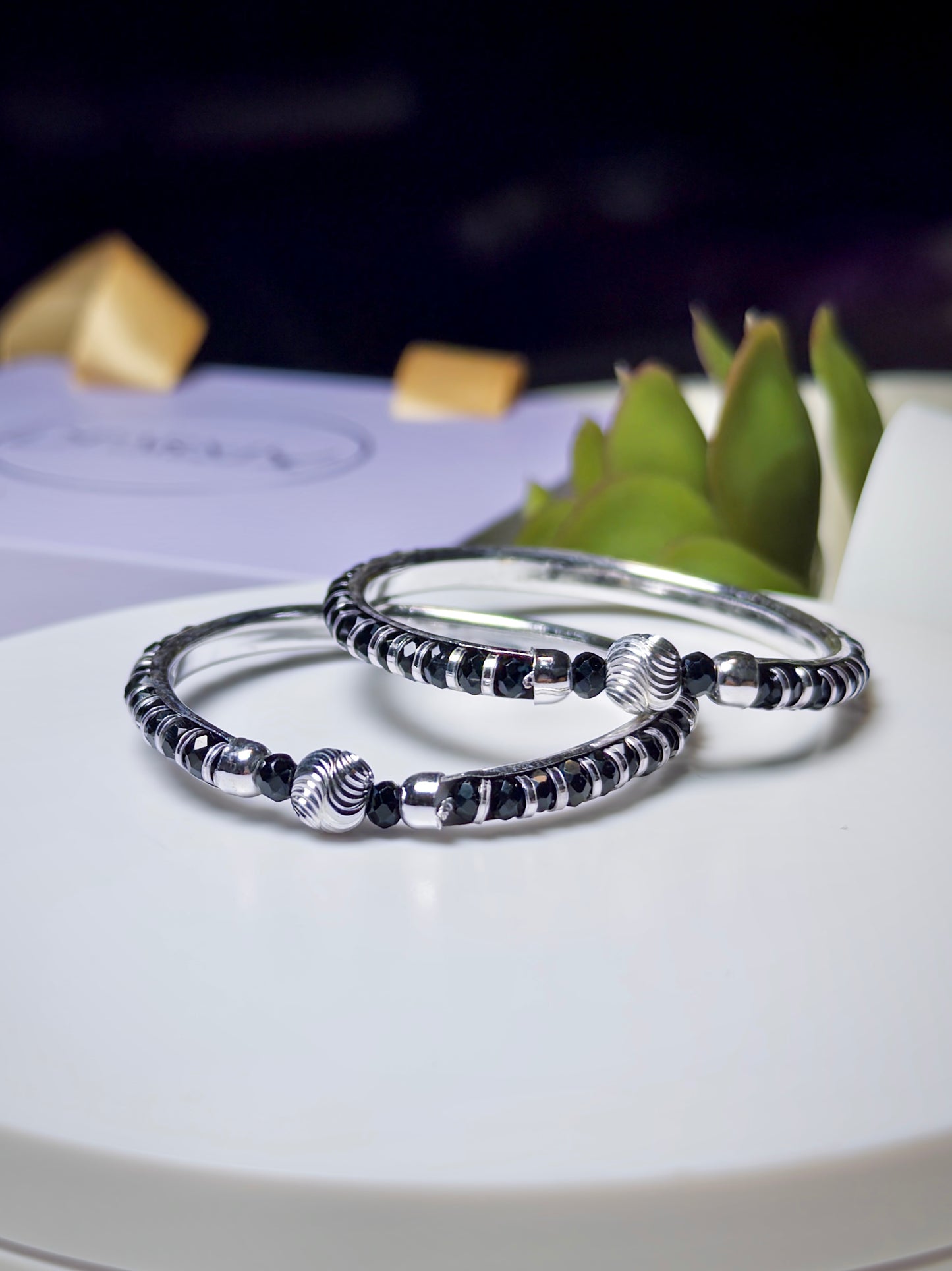 Silver baby bracelets with black beads on a white surface with a blurred background