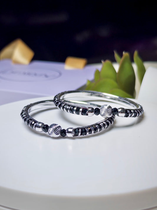 Silver baby bracelets with black beads on a white surface with a blurred background