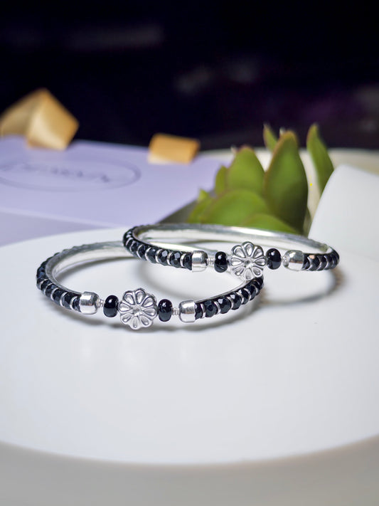 Two silver baby bracelets with black beads on a white surface with a blurred background