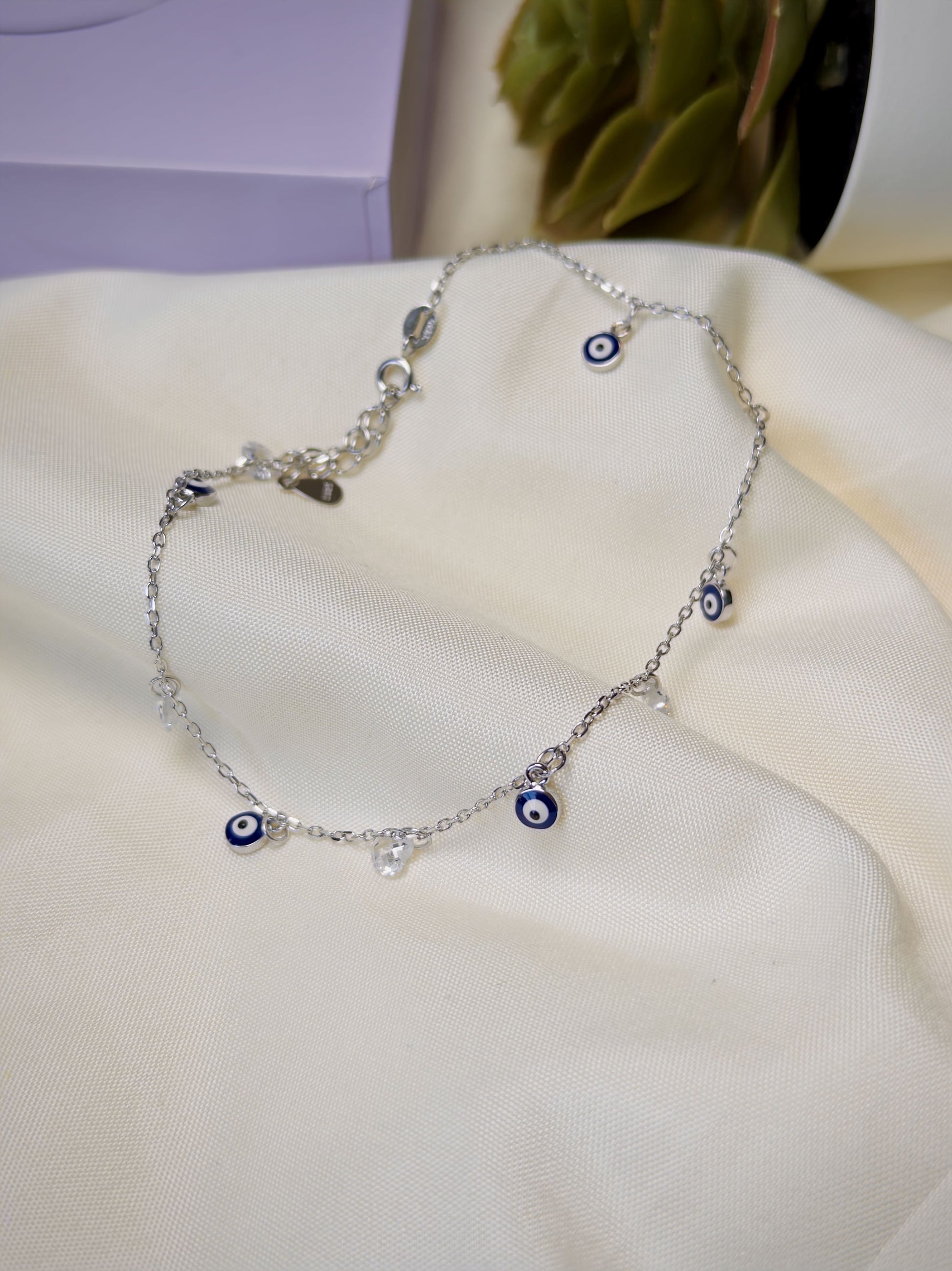 Silver anklet with blue evil eye charms on a white surface