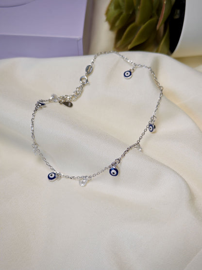 Silver anklet with blue evil eye charms on a white surface