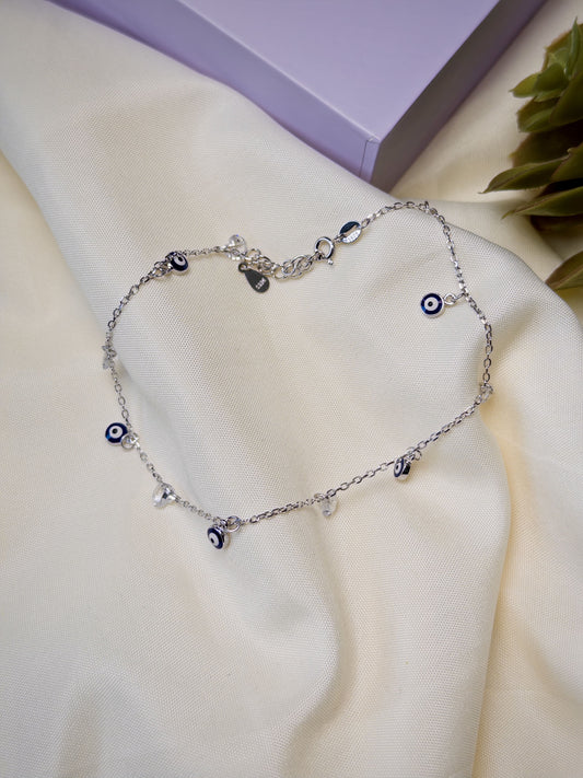 Silver anklet with evil eye charms on a white surface.