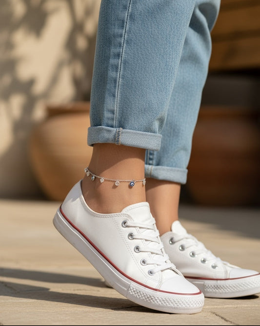 Silver evil eye anklet worn with light blue jeans on a wooden floor.