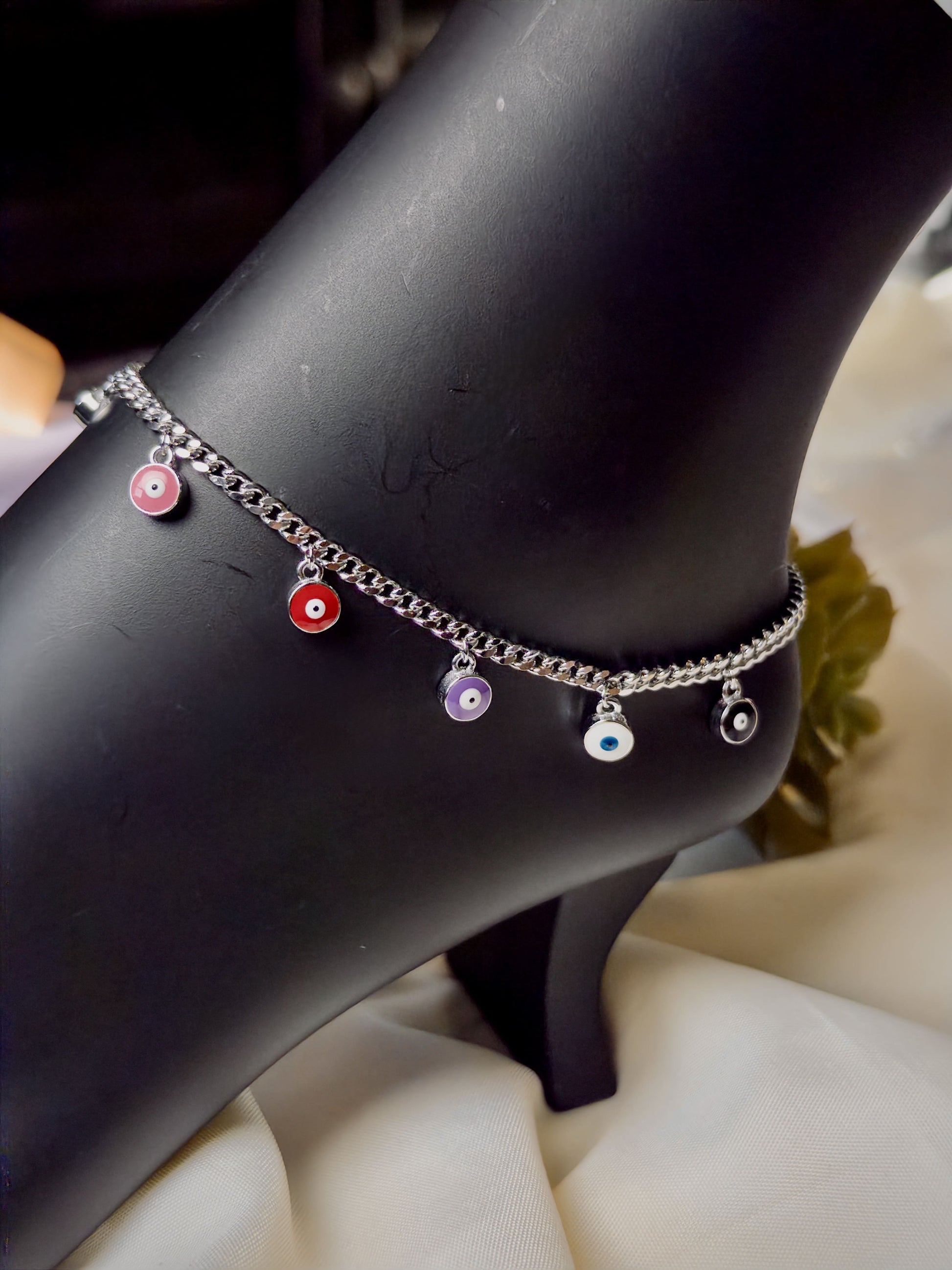 Silver anklet with colorful evil eye on a black mannequin foot.