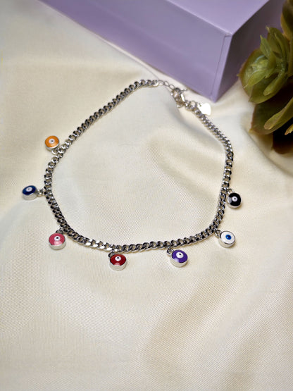 Silver chain anklet with colorful eye-shaped charms on a light fabric background