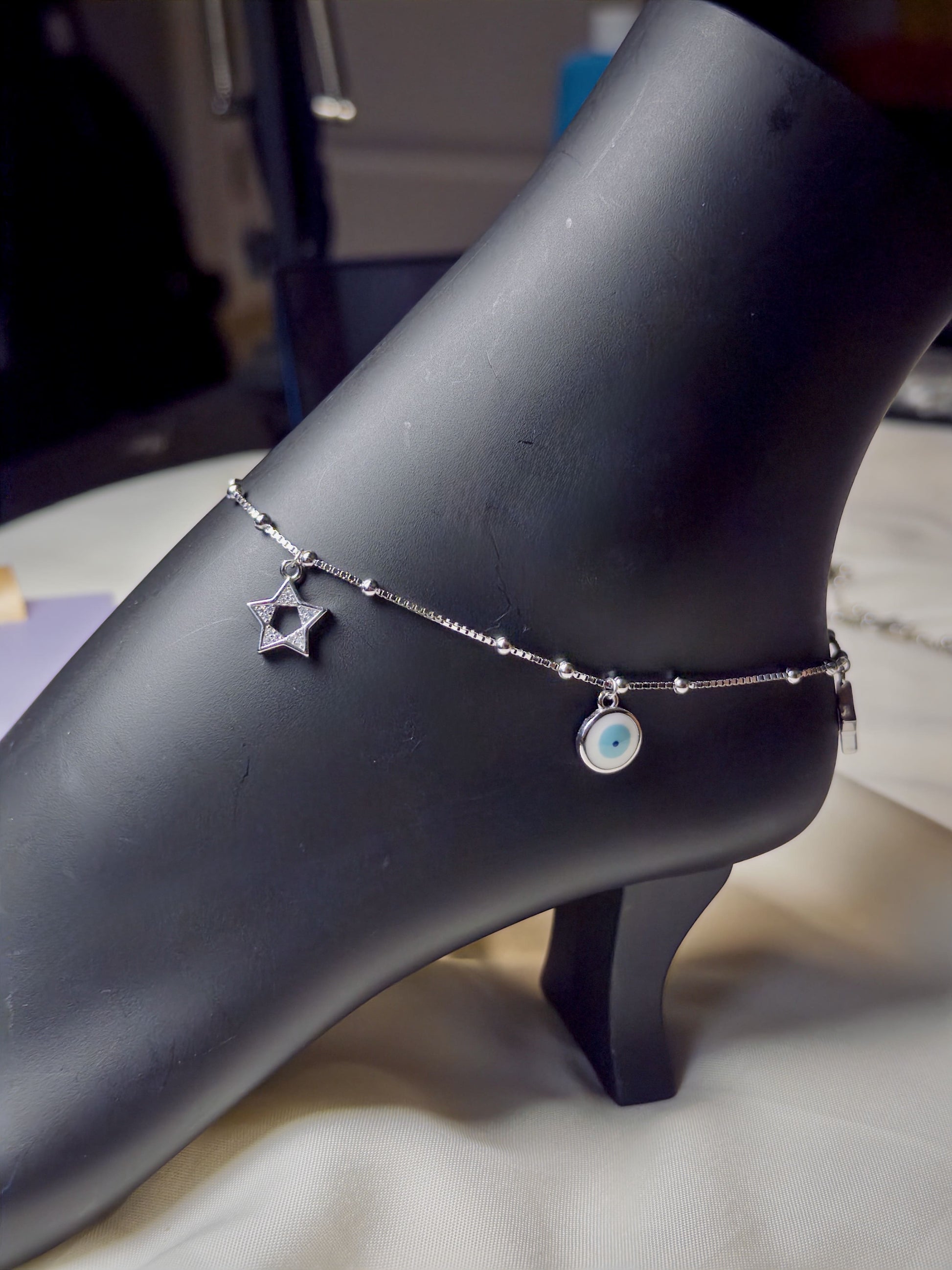 Silver anklets with star and heart charms on a mannequin foot.
