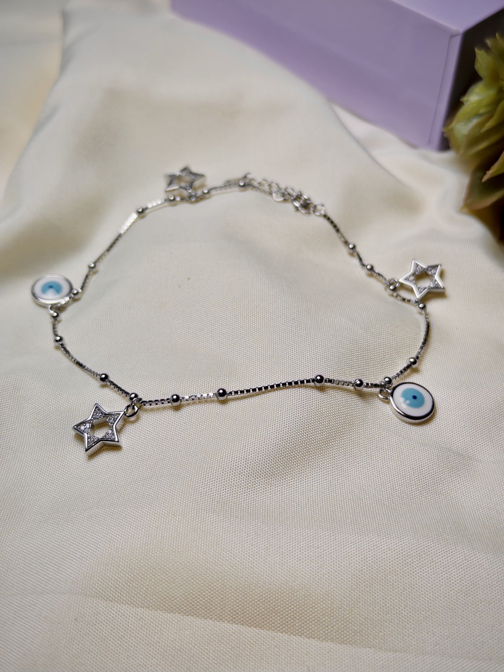 Silver bracelet with star and eye charms on a light fabric background