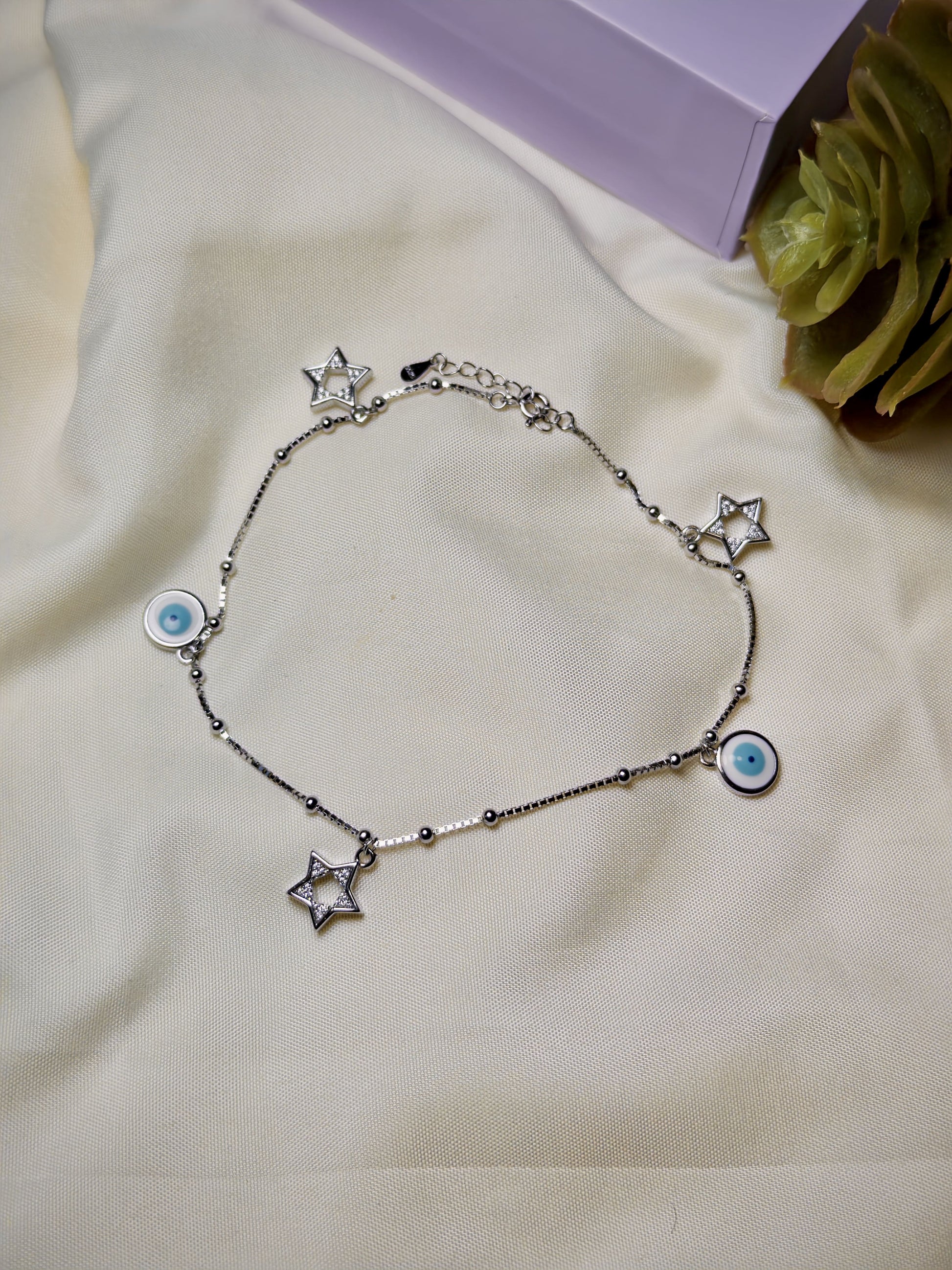 Silver bracelet with star and eye-shaped charms on a beige surface