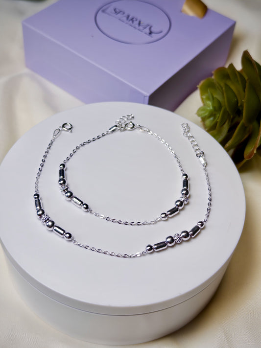 Kids silver anklets on a white stand with a purple box in the background