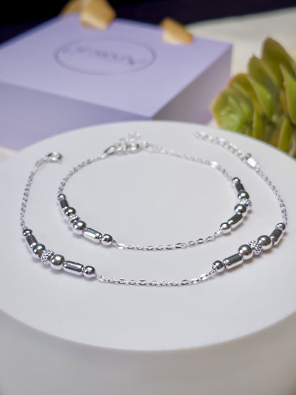 Silver anklets for kids on a white surface with a purple box in the background