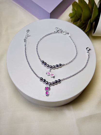 Silver anklets for kids with pink heart charm on a white surface