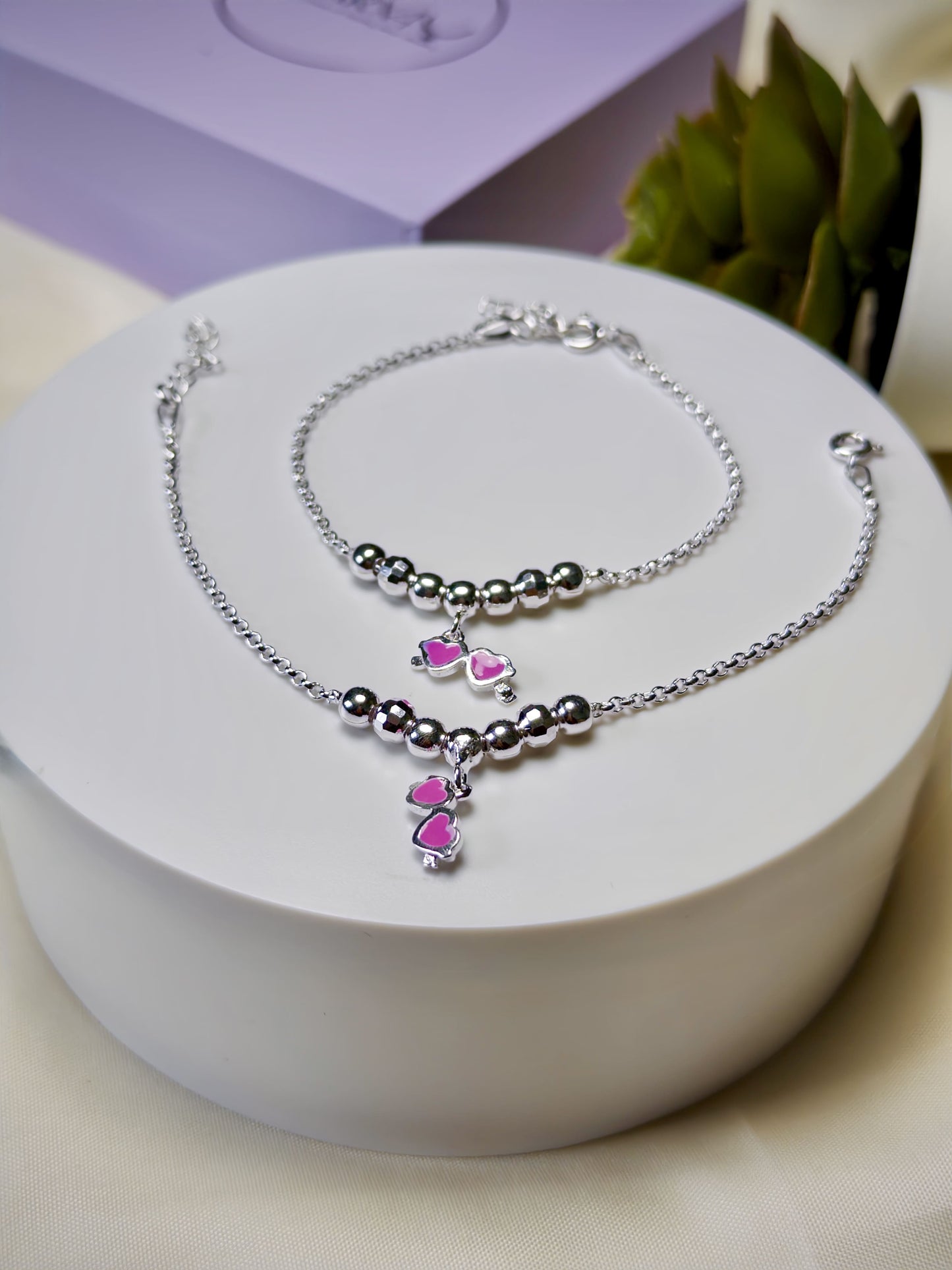 Kids silver anklets with heart-shaped charms on a white surface