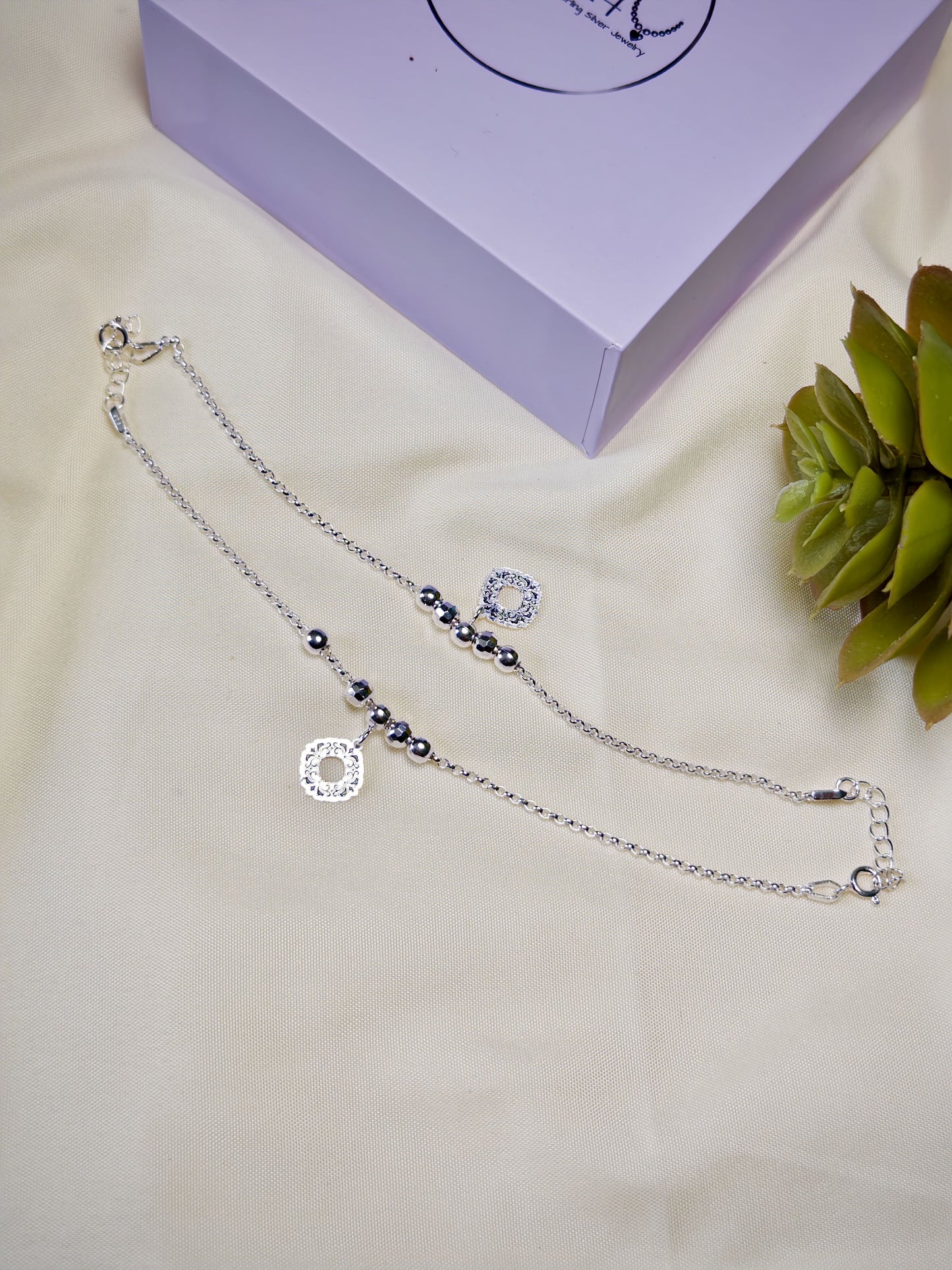 Kids silver anklets with beads on a beige surface with a purple box in the background
