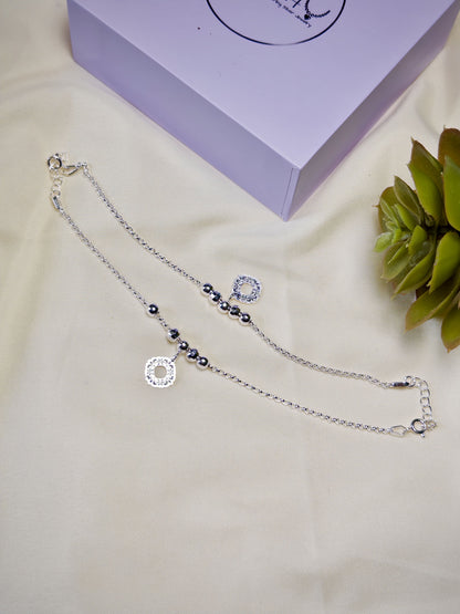 Kids silver anklets with beads on a beige surface with a purple box in the background