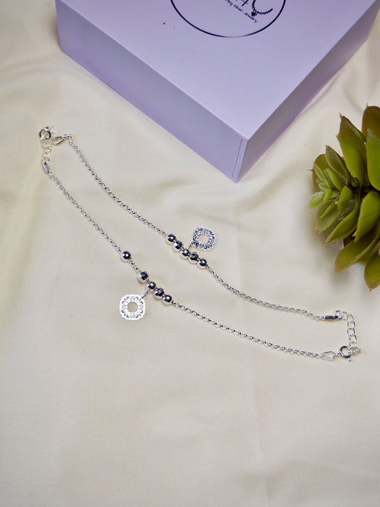 Kids silver anklets with beads on a beige surface with a purple box in the background