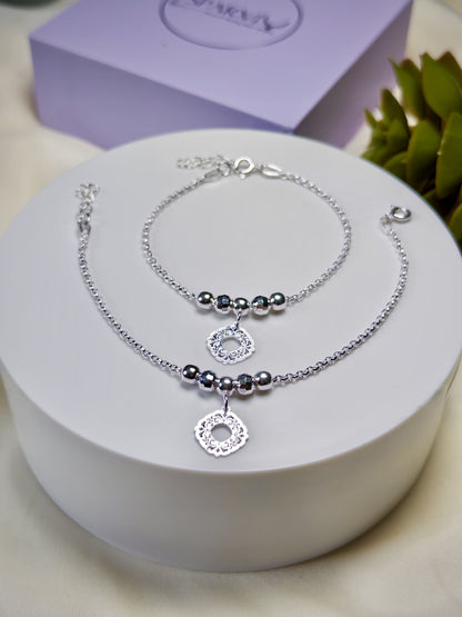 Kids silver anklets with silver beads on a white surface with a purple box in the background