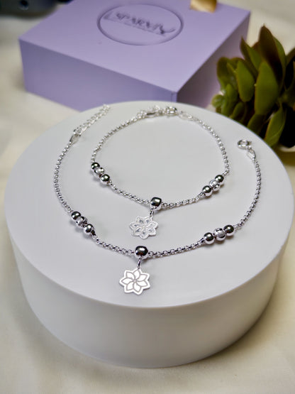 Kids silver anklets with floral charm on a white stand, with a purple box in the background.