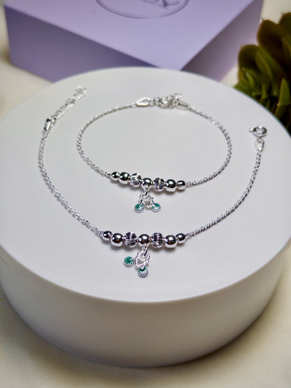 Kids silver anklets with green charms on a white surface