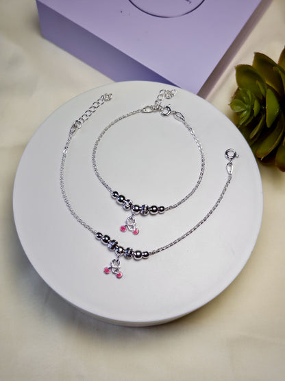 Kids silver anklets with beads and charms on a white plate, with a purple box and plant in the background.