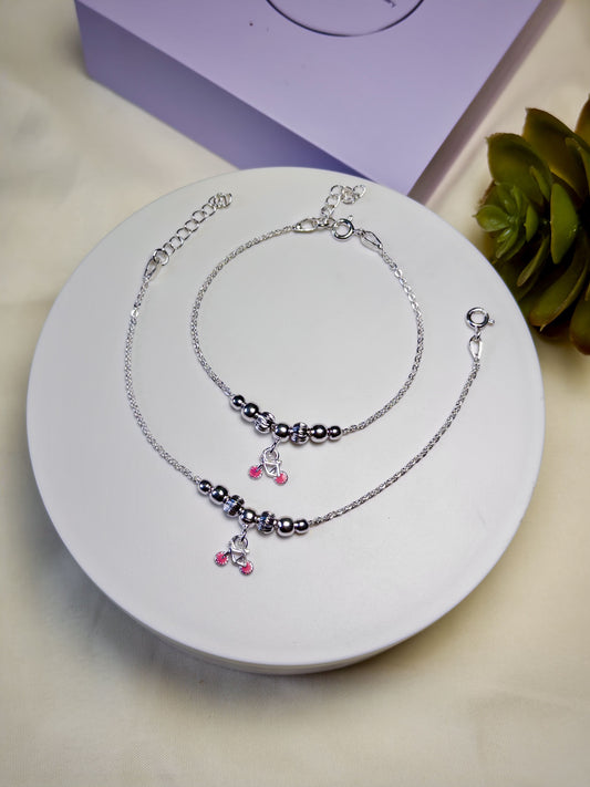 Kids silver anklets with beads and charms on a white plate, with a purple box and plant in the background.