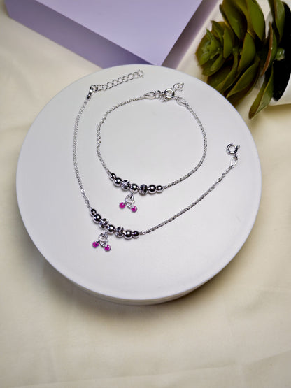 Set of kids silver anklets with purple charm on a white plate