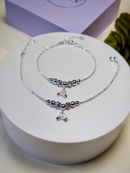 Kids silver anklets with red charms on a white stand with a purple box in the background