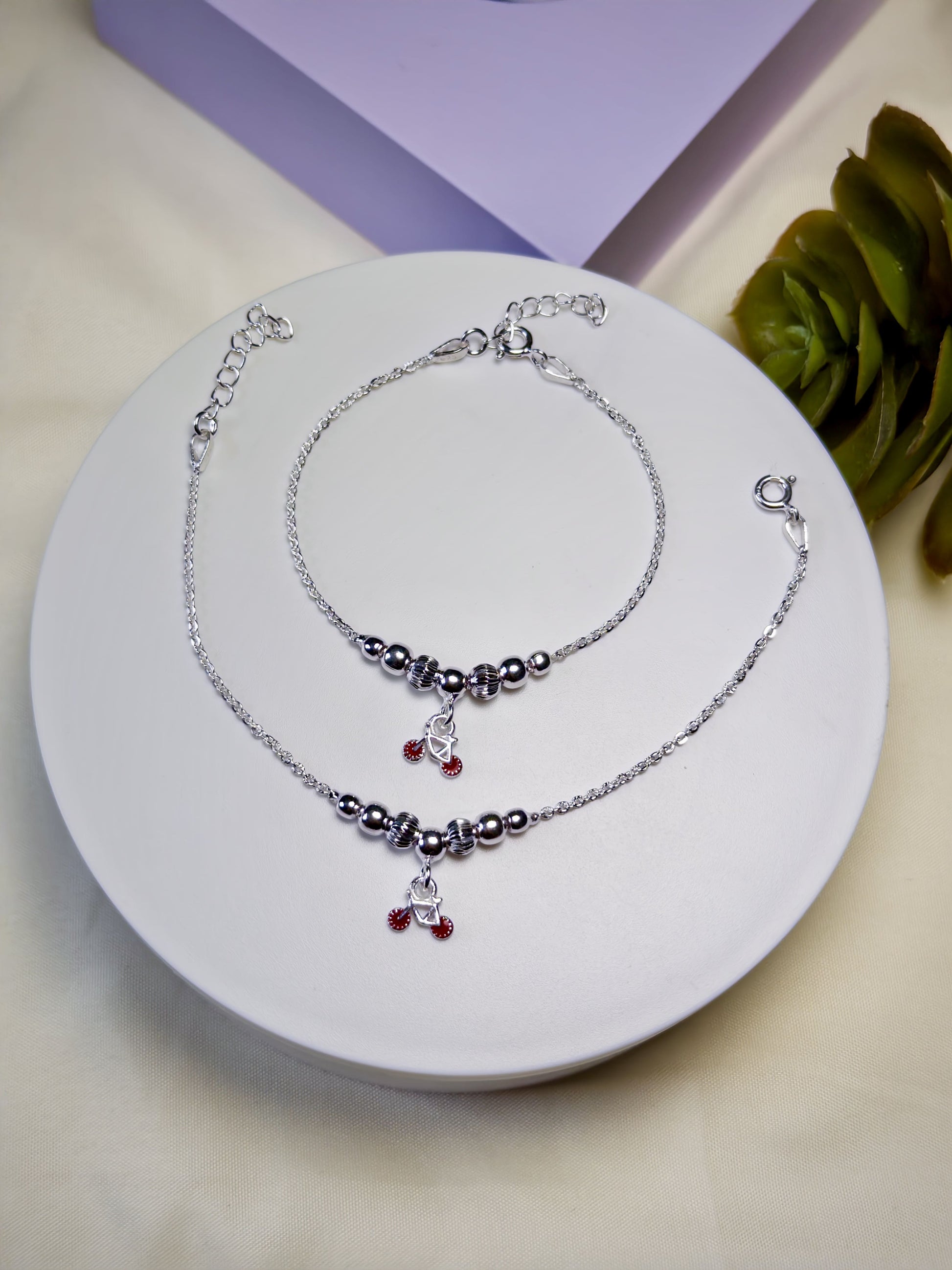 Kids silver anklets with red beads on a white plate