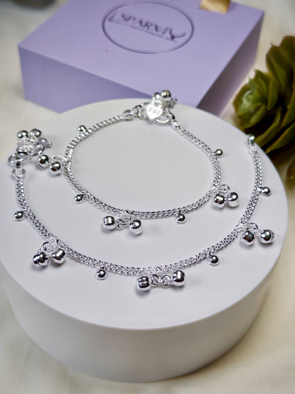 Kids silver anklets with heart-shaped charms on a white surface with a purple box in the background