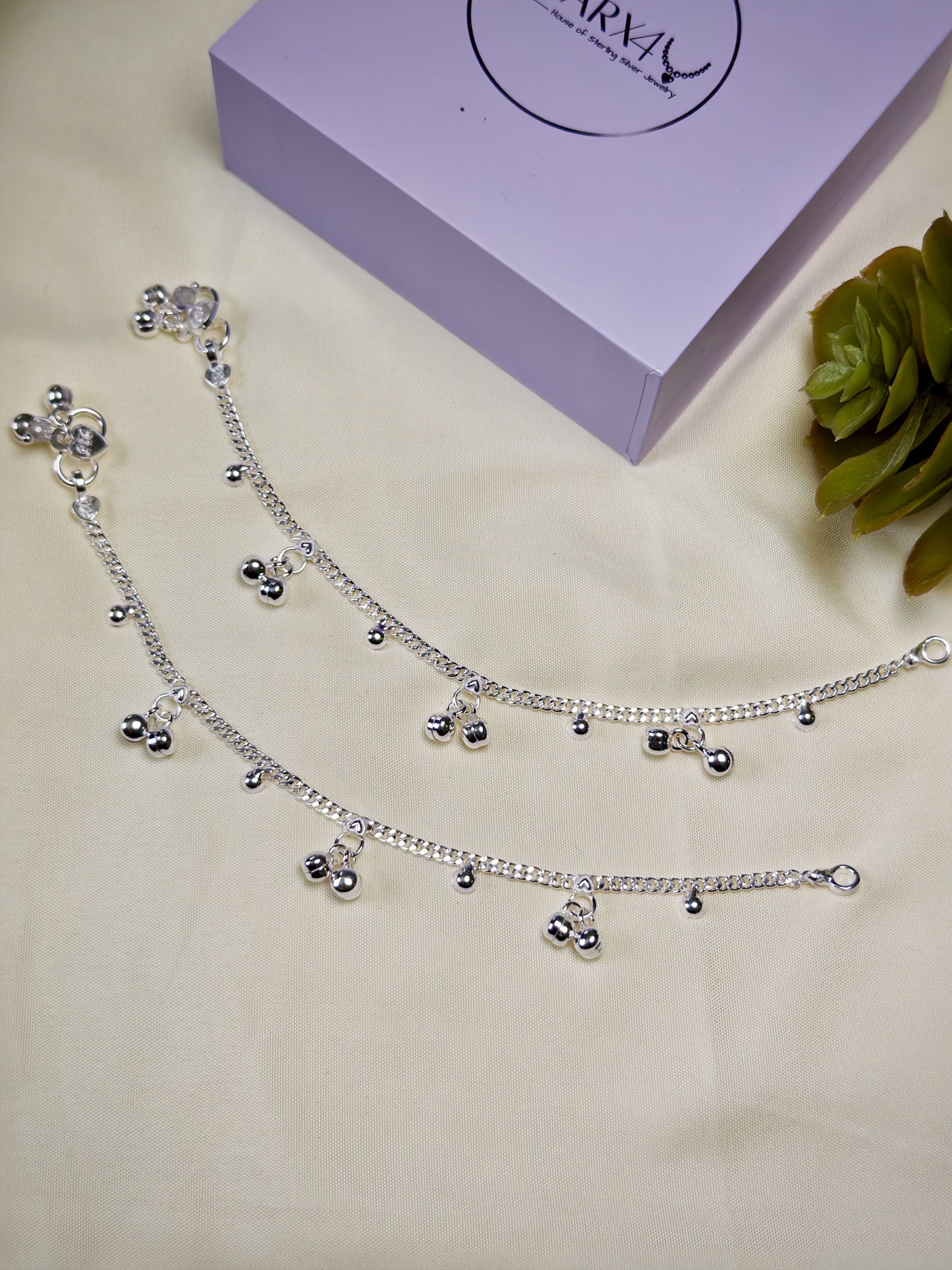 Kids silver anklet with charms on a light surface next to a purple box.