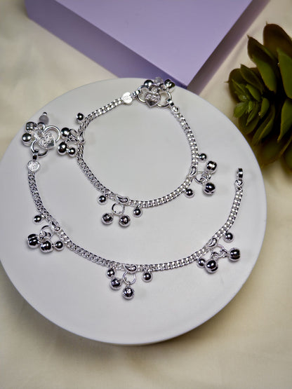 Kids silver anklets with charms on a white plate with a purple box and green leaves in the background
